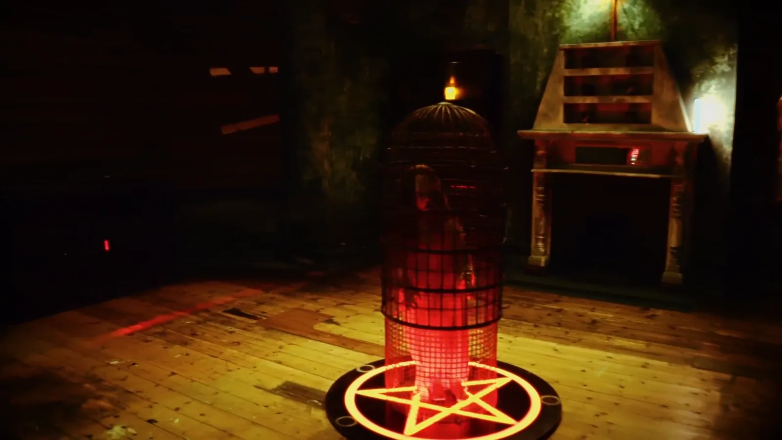 A caged figure glowing red above a pentagram in the parlour of The Haunting
